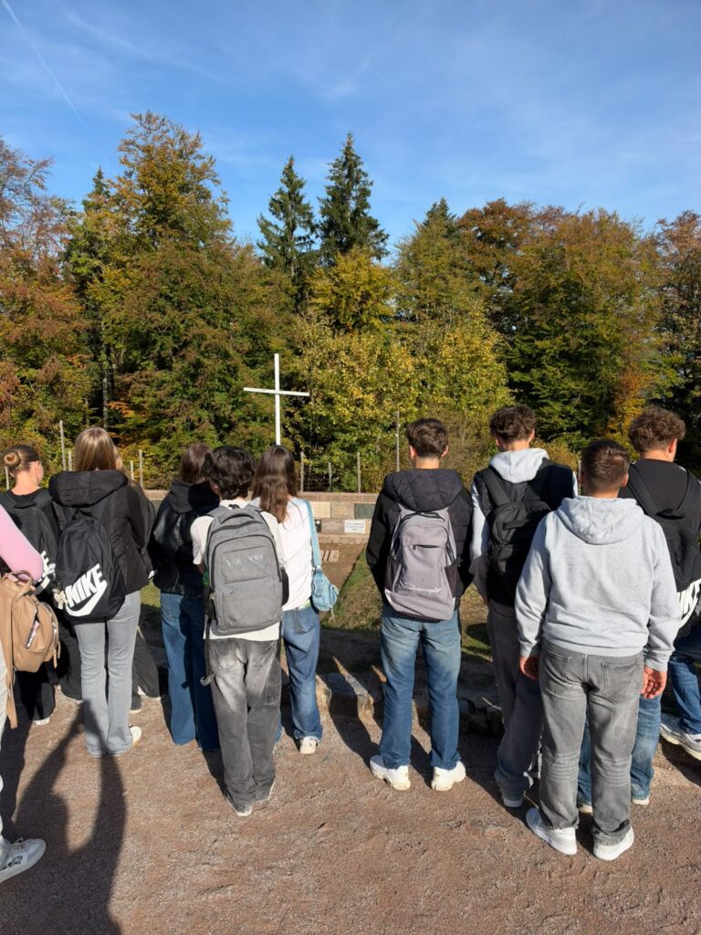 Schülerinnen und Schüler der 10. Klassen stehen an der Gedenkstätte Natzweiler-Struthof vor einem weißen Kreuz