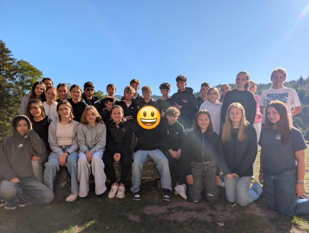 Gruppenfoto einer 8. Klasse im Freien vor Bäumen und blauem Himmel